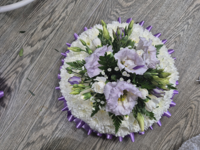 Massed Posy - A graceful and elegant tribute featuring a soft palette of white and lavender tones, beautifully finished with a coordinating satin ribbon edge.